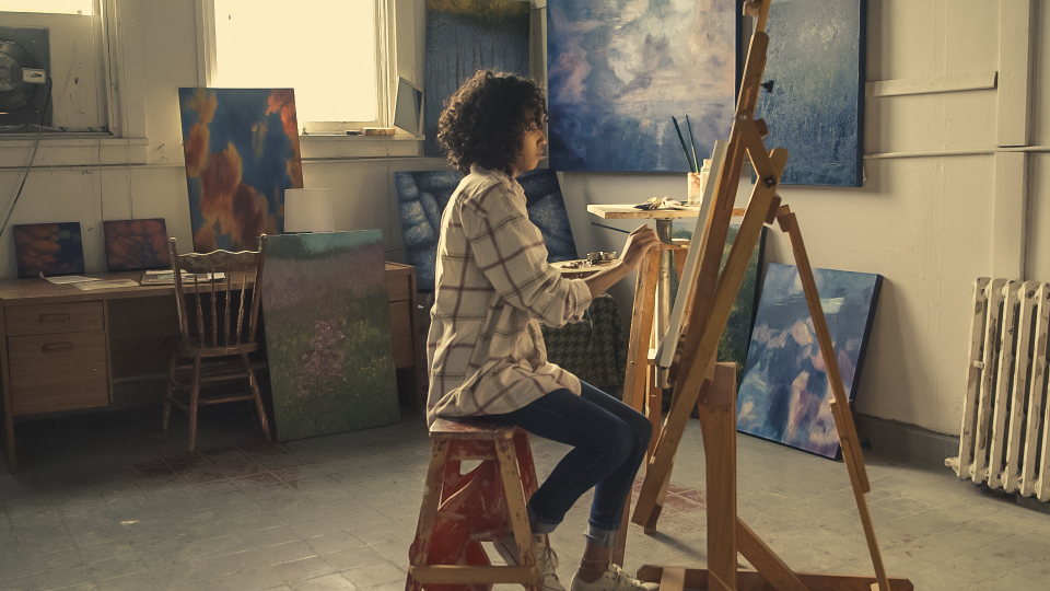 Grady Vest's painting area with easel, brushes, and works in progress